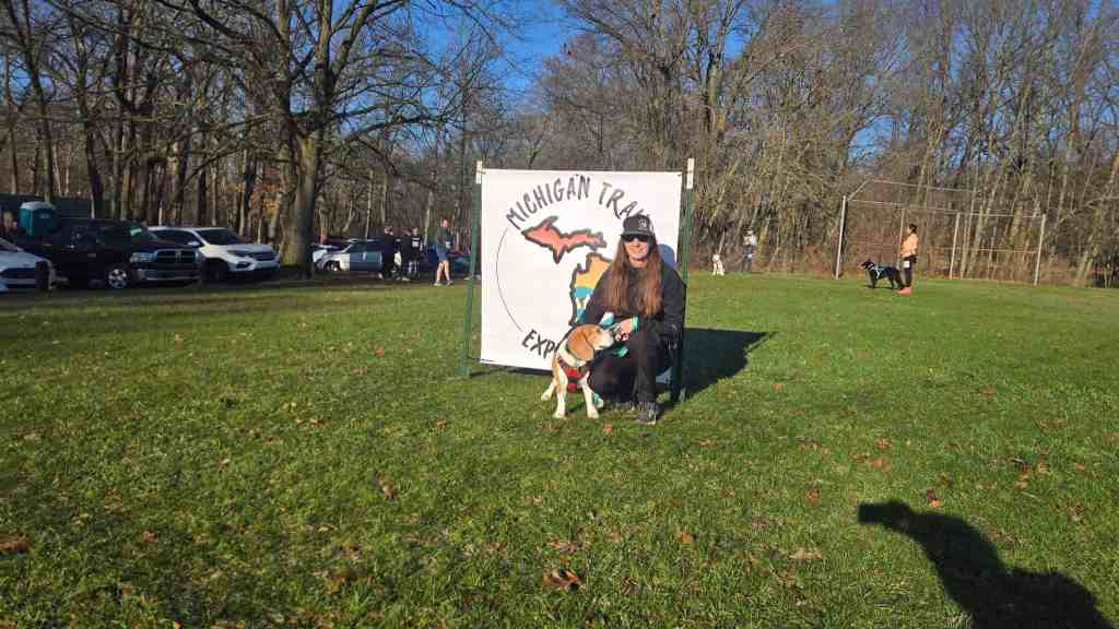 Amie and Dakota in front of the Michigan Trail Experience sign at Spring Trail Trot 5K