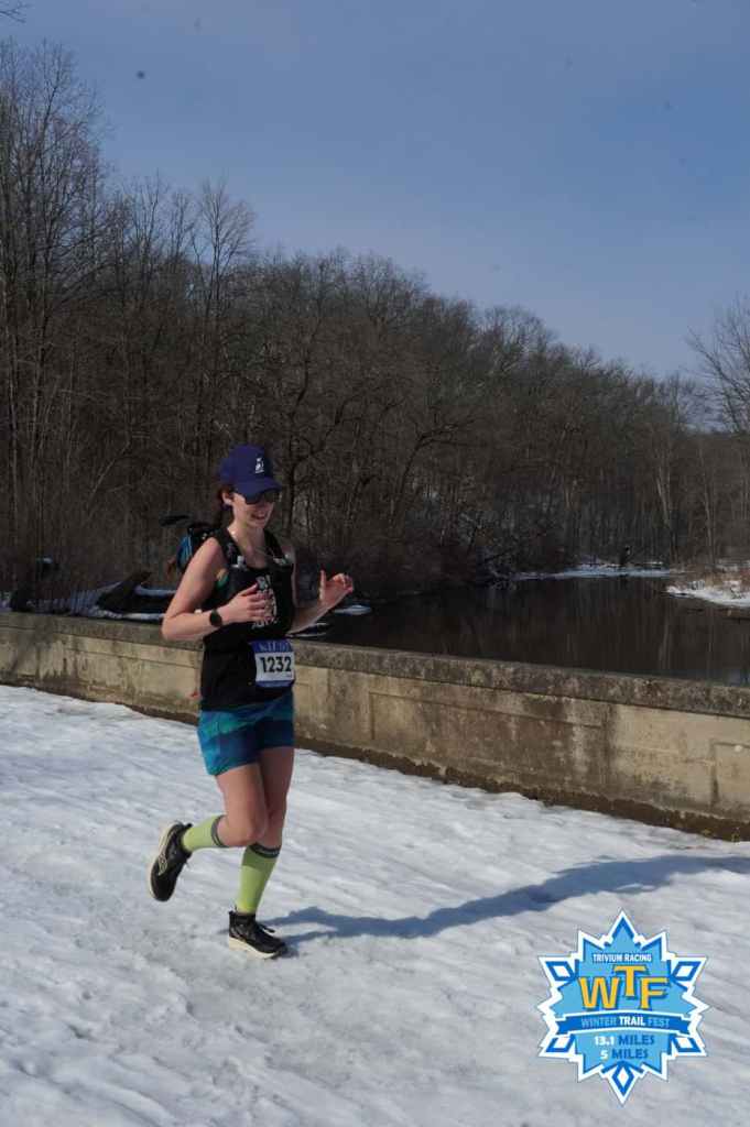 Amie smiling running across a bridge at Winter Trail Fest