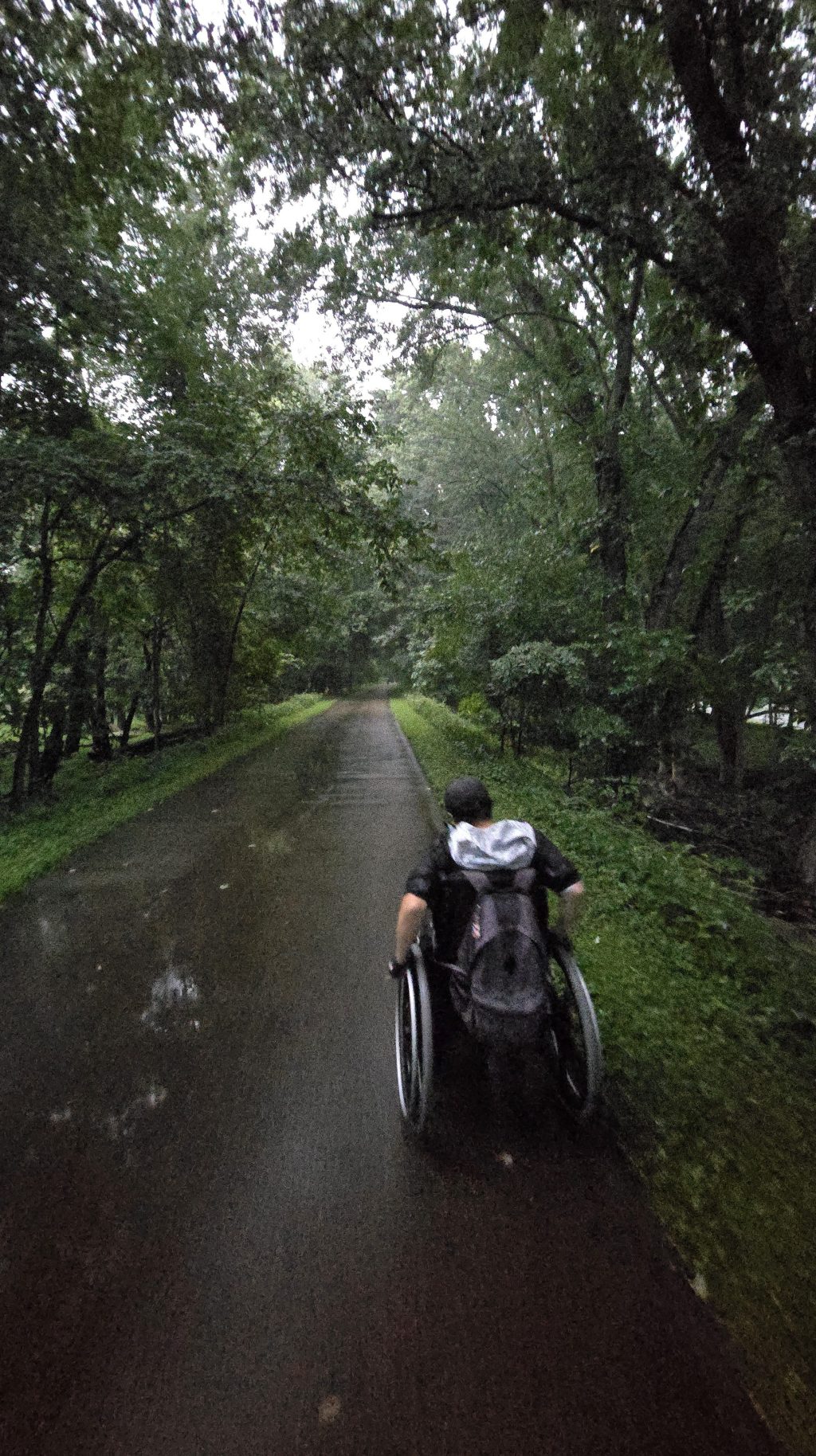Dustin enduring the rain and pushing along a wet, paved path